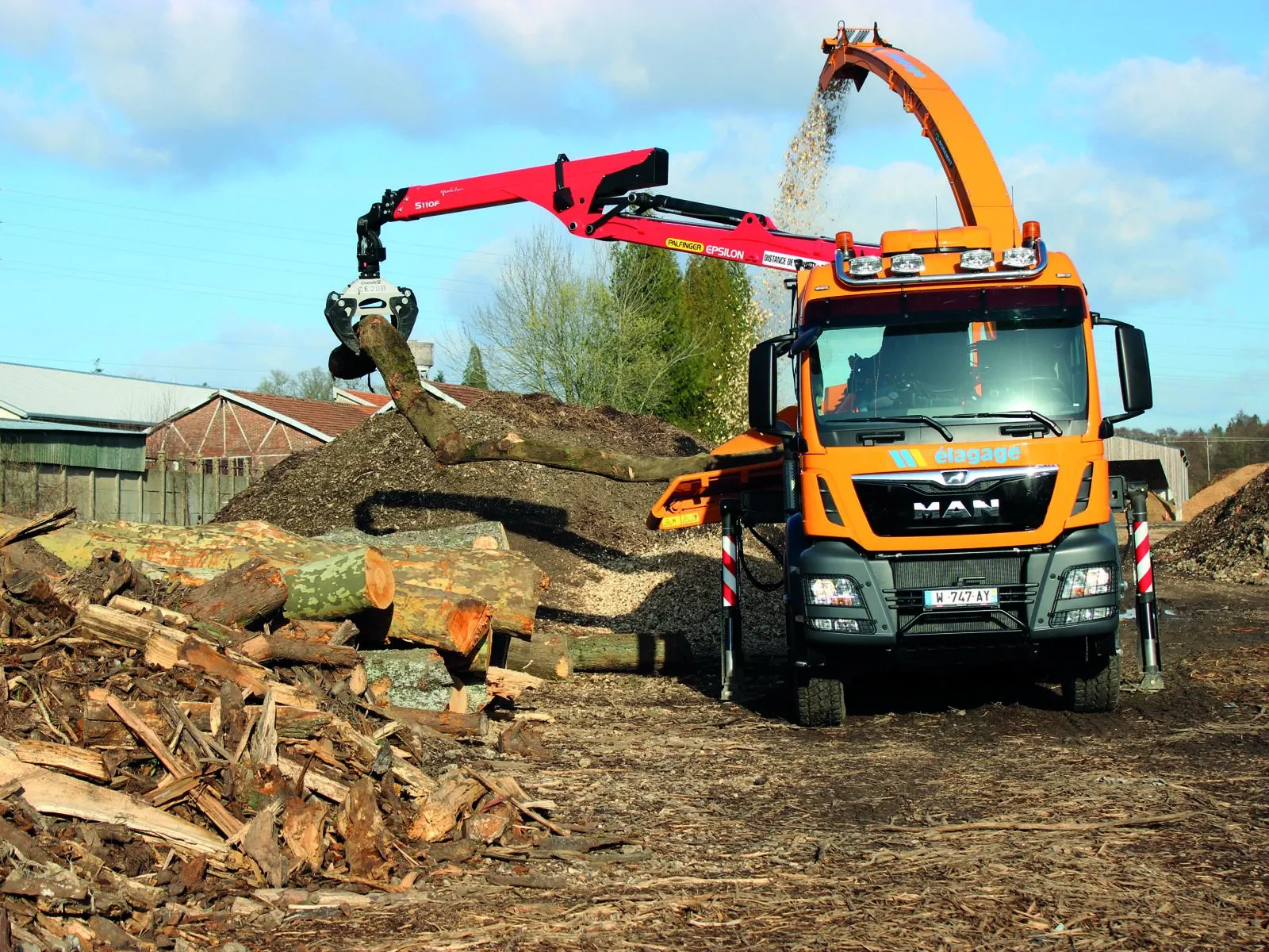 Camion-grue chargeant des grumes dans une déchiqueteuse sur chantier
