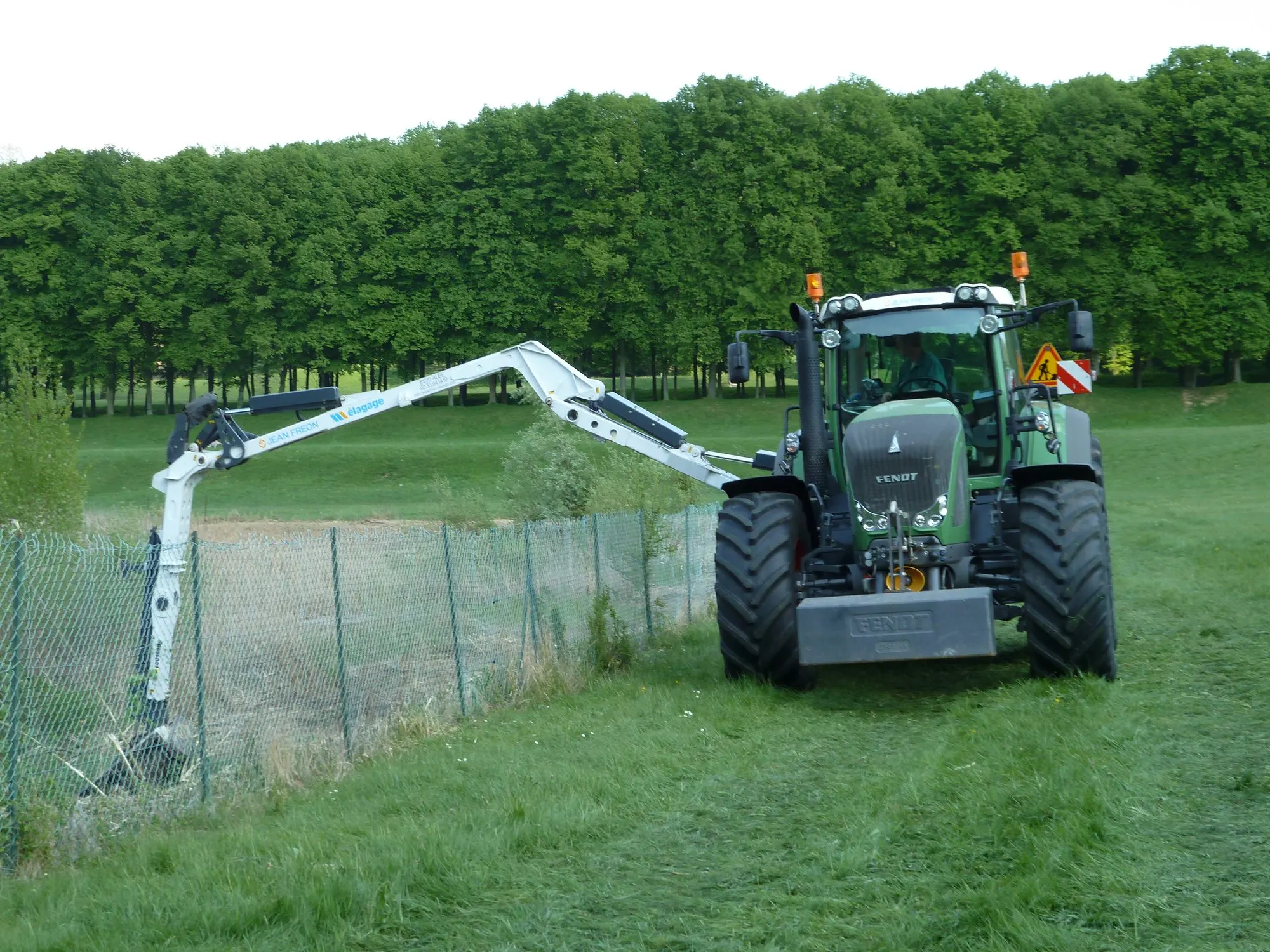 Tracteur équipé d'un lamier taillant une haie le long d'une clôture