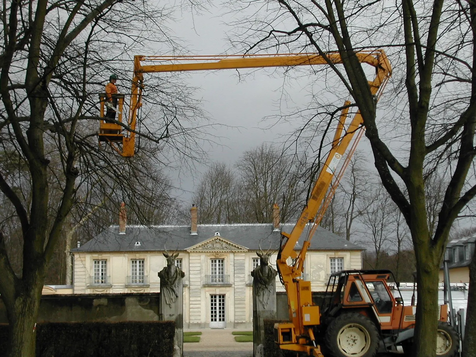 Nacelle orange élaguant des arbres devant un manoir